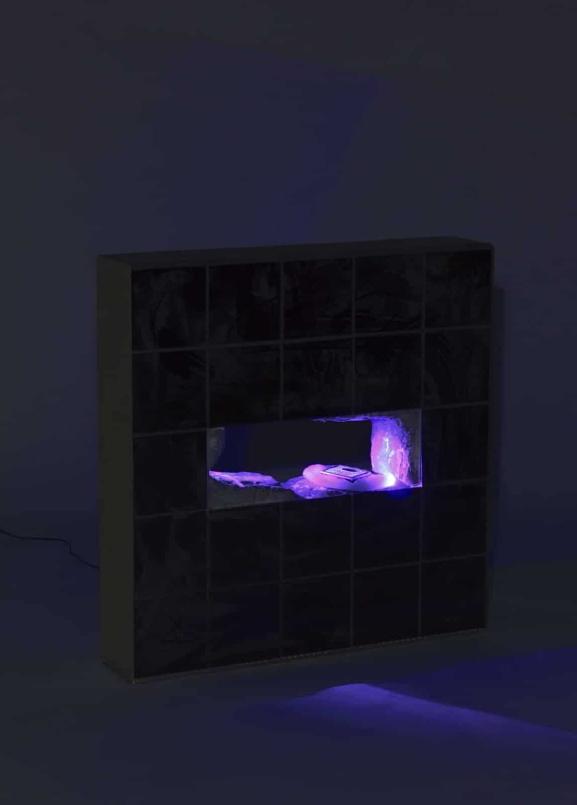 A medium height sculpture covered with tiles and a hole with a harddrive and lights